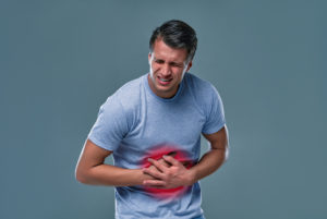 A man touching his stomach, on gray background with copy space. Stomach pain and others stomach disease concept.