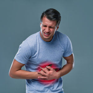 A man touching his stomach, on gray background with copy space. Stomach pain and others stomach disease concept.